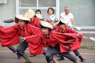 赤い衣装に笠をかぶった子供たちが、かがんで両手を広げ、踊っている写真