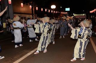 笠をかぶった浴衣姿の人たちが、盆踊りをしながら練り歩いている写真