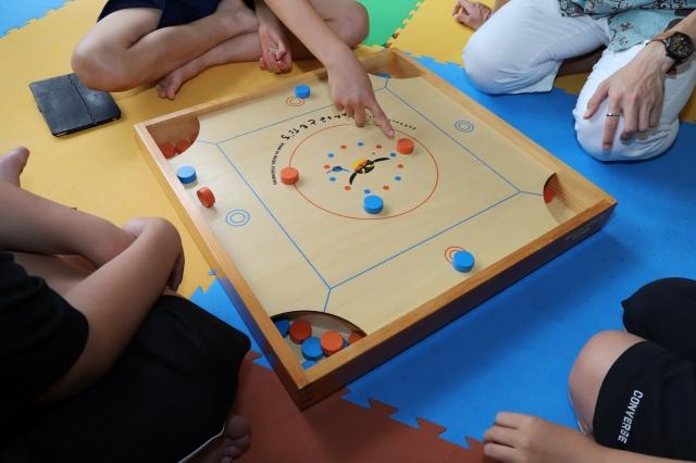 浅い箱の中で、子どもの手がオレンジ色の駒を指さしている写真