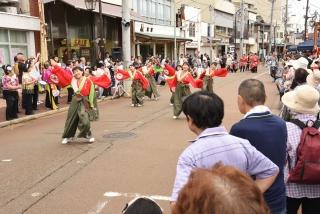 赤とカーキ色の衣装を着た人たちが、両手を振り上げて踊り歩いている写真