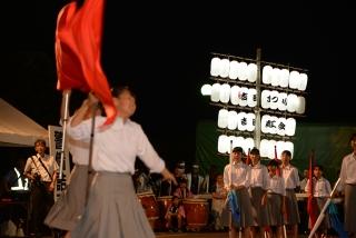 赤い旗を持ち上げて踊る女子中学生たちと、それを見ている中学生たちの写真