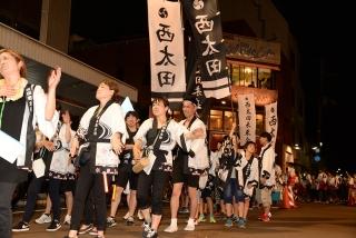 白と黒のはっぴを着た人たちが、路上を練り歩いている写真