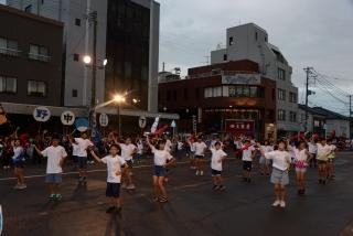 夕暮れ時に、路上で白いTシャツを着た子供たちが並んで踊っている写真