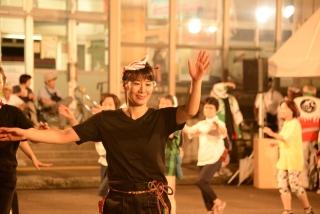 黒いシャツに紅白のお面をつけた女性が、両手を振って踊っている写真
