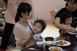 赤ちゃんを抱っこしながら出来上がった料理を食べる女性の写真