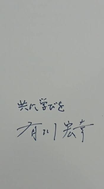 紙に青いインクで「共に学びを 有川宏幸」と直筆サインがされている様子を収めた写真
