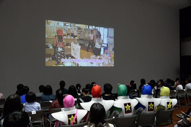 並べられた椅子に座ったたくさんの子ども達が見ている、スクリーンに映し出された動画の写真
