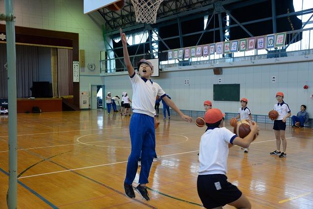 体育館内で、バスケットゴールにボールをジャンプしながら放っている男子生徒の写真
