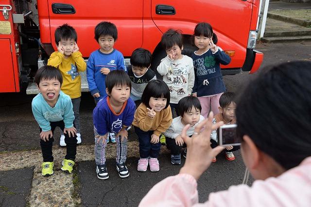 消防車の前で、前後二列に並び保育士に写真撮影をしてもらっている園児達10人の写真