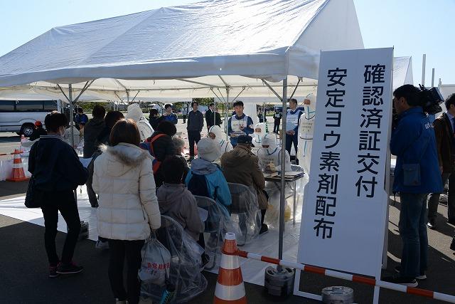 「確認済証交付 安定ヨウ素剤配布」と書かれた白い看板の前で列になって並んでいる参加者の写真