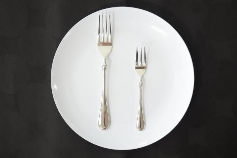 黒いテーブルクロス、白いお皿、大小二つのサイズのフォークが並んだ写真