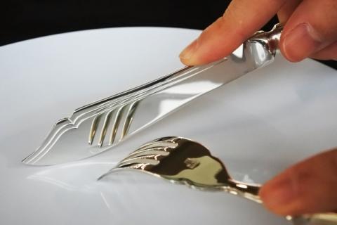白いお皿の上で、ナイフとフォークを構えている手のアップの写真