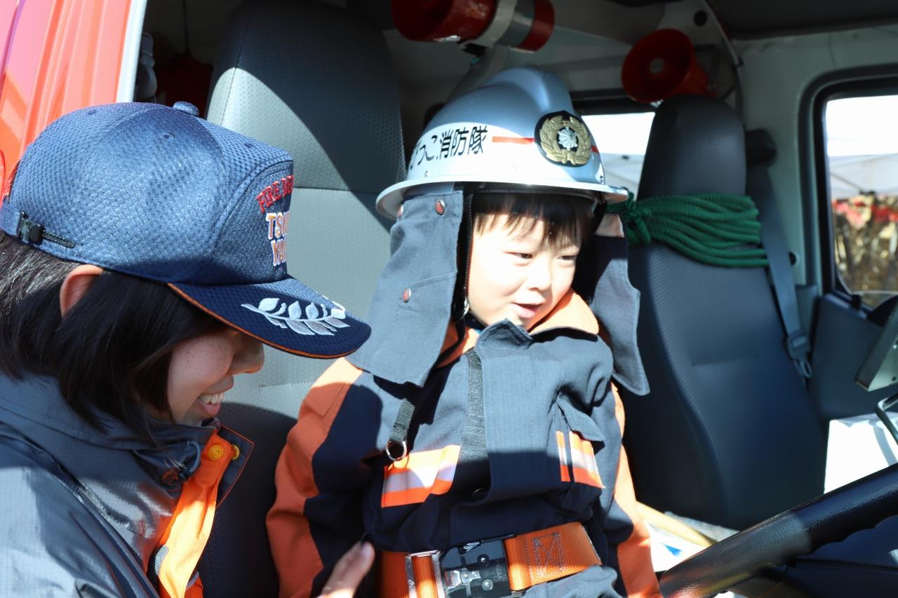 消防隊服を着て消防車の中に入る児童の写真