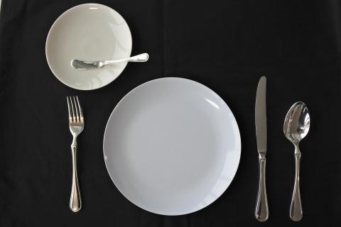黒いテーブルクロスの上に並んだ白い二つのお皿とシルバーのカトラリーの写真