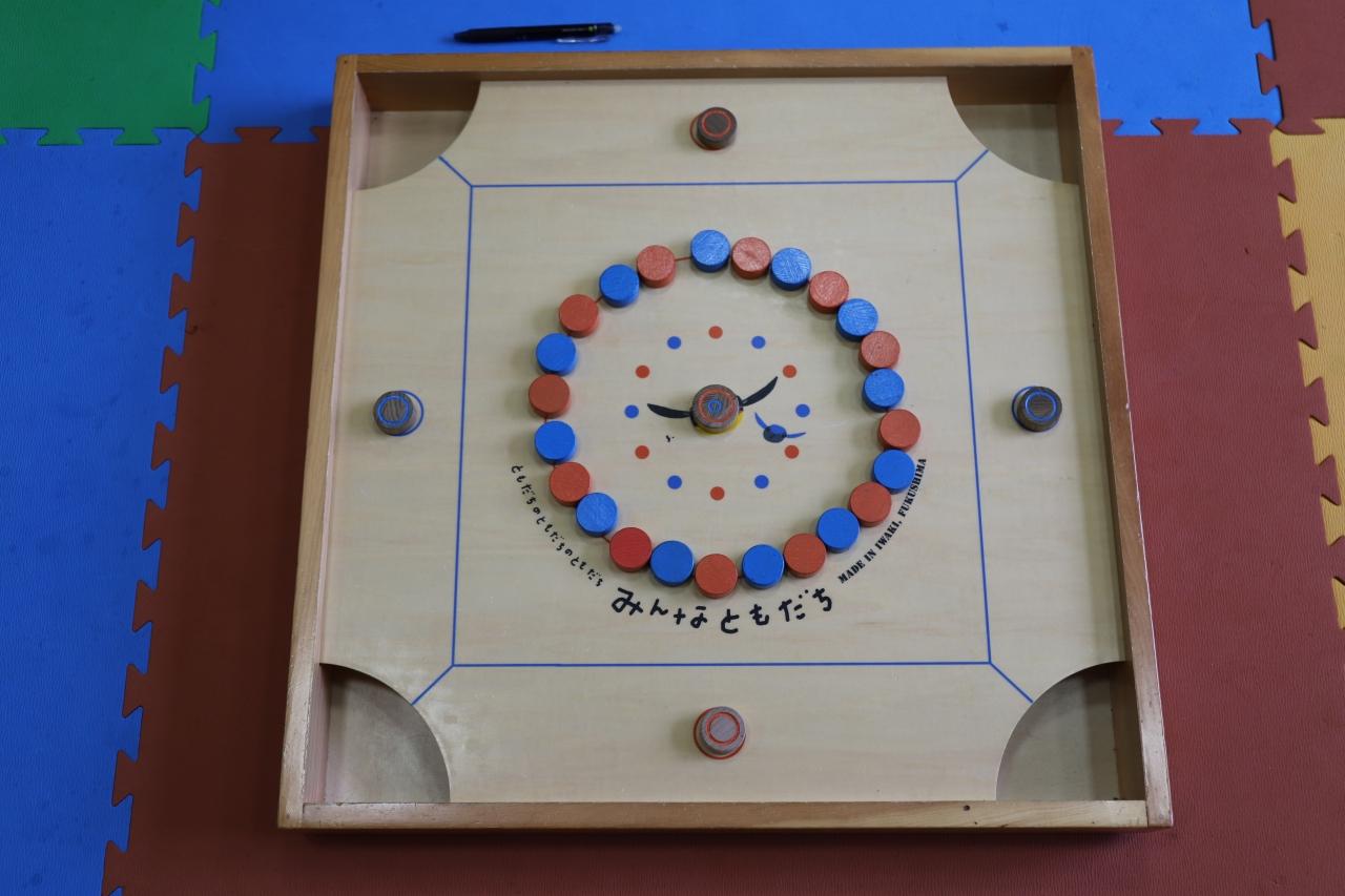 赤と青のコマが円状に並べられていて中心にみんなともだちと書かれてあるボードゲームカロムの台の写真v