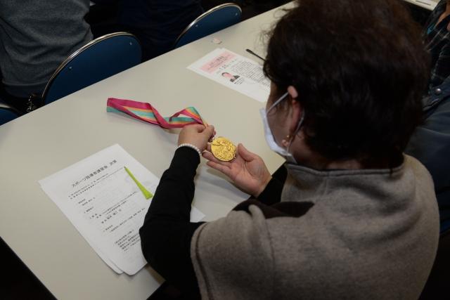 参加者に回覧された金メダルとそれを手に取って観察する女性参加者の写真