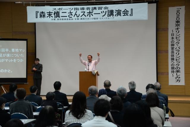 壇上で両手を上げユーモアを交えながら講演している森末慎二さんと参加者たちの様子