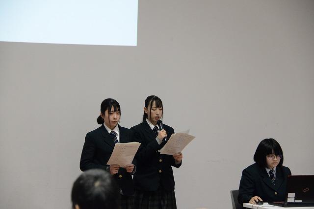 マイクと書類を手に発表をしている女子生徒二人と、その横にある机上のPCを操作している眼鏡の女子生徒の写真