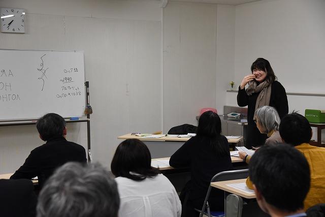 着席している参加者を前に、口元を手で指し発音の仕方を教えている女性の写真