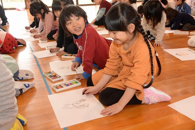 床に座って隣の子と楽しそうに喋りながら菅原道真の絵をクレヨンで描いている子ども達の写真