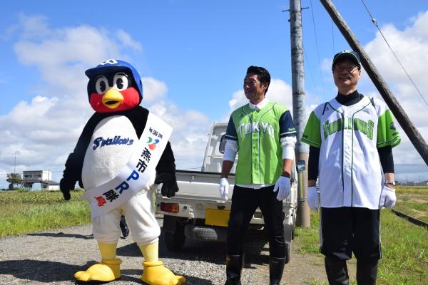 水田の前にいる関係者2人と東京ヤクルトスワローズマスコットキャラクターつば九郎の写真