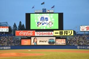 野球の試合時のバックスクリーンに緑色をバックとして燕市の燕と花魁のキャラクターと「燕市」と表示されている写真