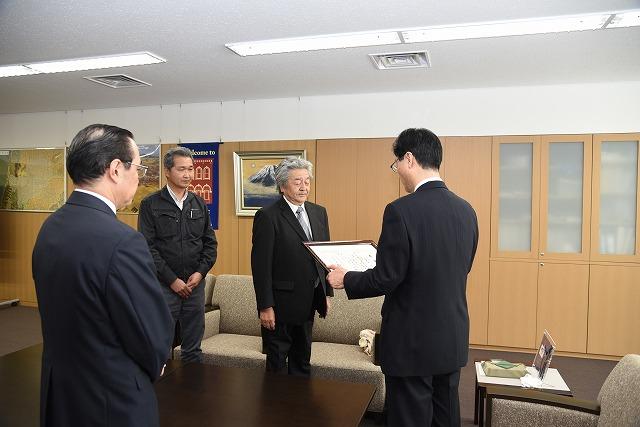 執務室に立っている二人の男性に対し、感謝状を読み上げている市長の写真