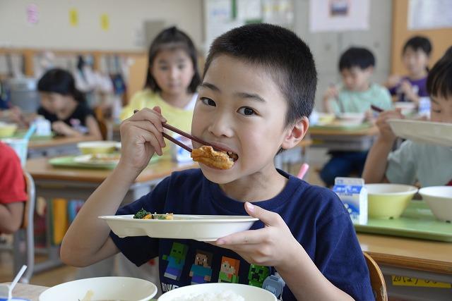 鶏肉のレモン和えを笑顔で食べる青いTシャツを着た男の子の写真