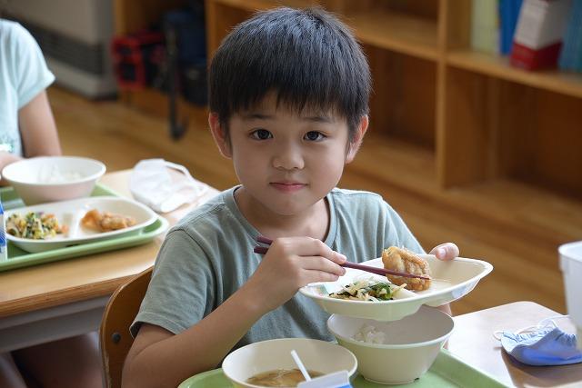 お皿の上の鶏肉のレモン和えを箸でつかみながらほほ笑むグレーのTシャツを着た男の子の写真