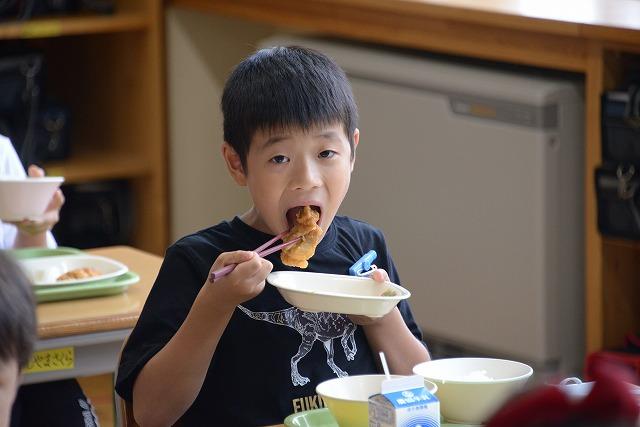 大きく口を開けて鶏肉のレモン和えにくらいつこうとしている様子の黒いTシャツを着た男の子の写真