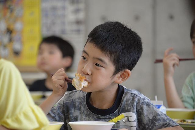 鶏肉のレモン和えに笑顔でかぶりつく男の子の写真