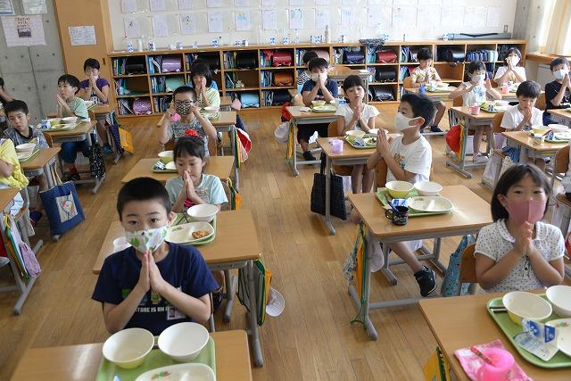 教室内に広げられた机と椅子に座り、食べ終えて空になった給食皿を前にごちそうさまのあいさつをしている子供たちの写真