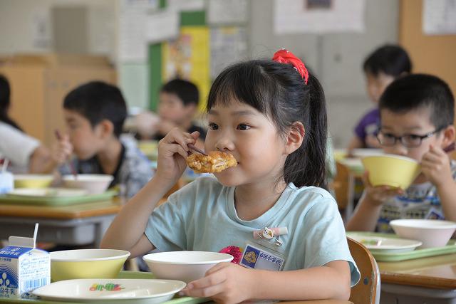 鶏肉のレモン和えを笑顔でほおばるグレーのTシャツを着た女の子の写真