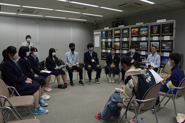 まちあそび部メンバーの学生たちに円卓上に座りながらインタビューを行う制服姿の人達の写真