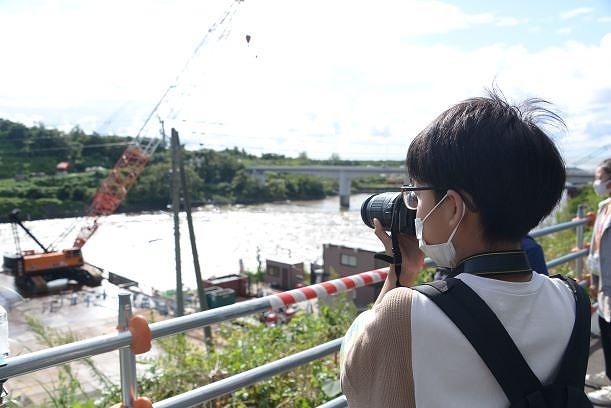河川とクレーンに向かってカメラを向ける男の子の写真