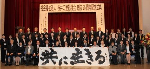 「共に生きる」という看板を前に置いた、ステージ前での「社会福祉法人 桜井の里福祉会」の方々の集合写真