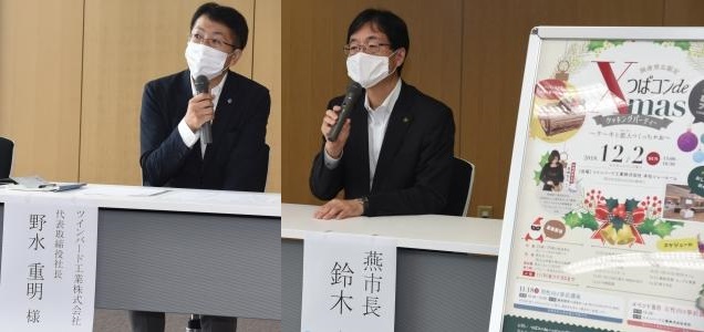 マスクをしながらマイクを手に持つスーツ姿の野水社長と鈴木市長の写真