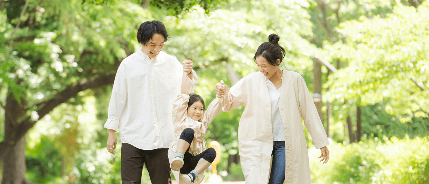 木漏れ日の中、父親と母親に両腕を持たれてブランコのように遊ぶ女の子