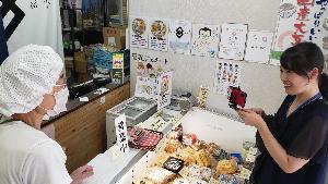 職員が嘉平豆腐店を訪問しオンラインまちあるきしていることを説明している様子